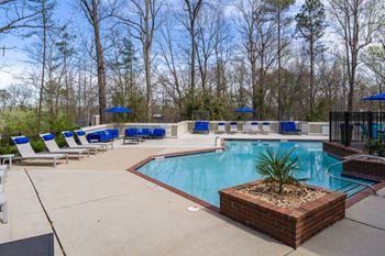 An outdoor pool and deck area with lounge chairs, surrounded by trees.